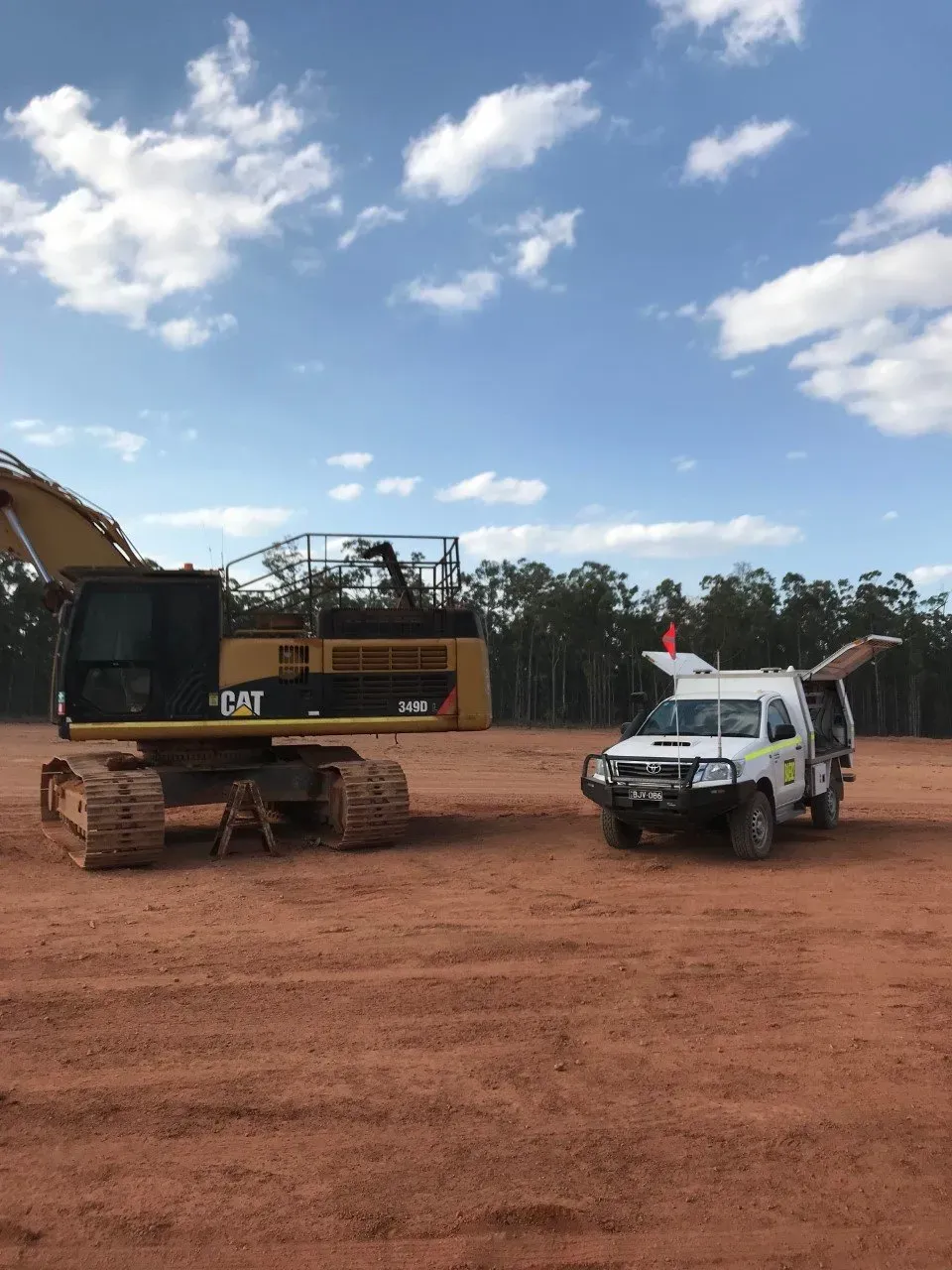 A Large Excavator Is Parked Next To A White Truck In A Dirt Field — Brad's Auto Electrical in Mareeba, QLD