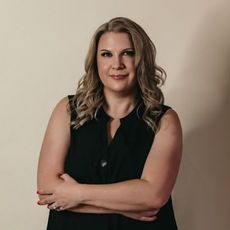 A woman in a black shirt is standing with her arms crossed.