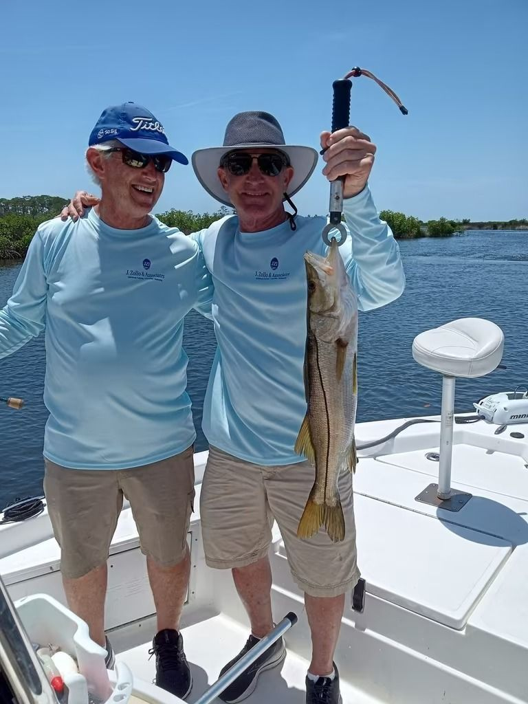 Two men on a boat smiling with a fish. One man holds the fish up. Blue sky and water.