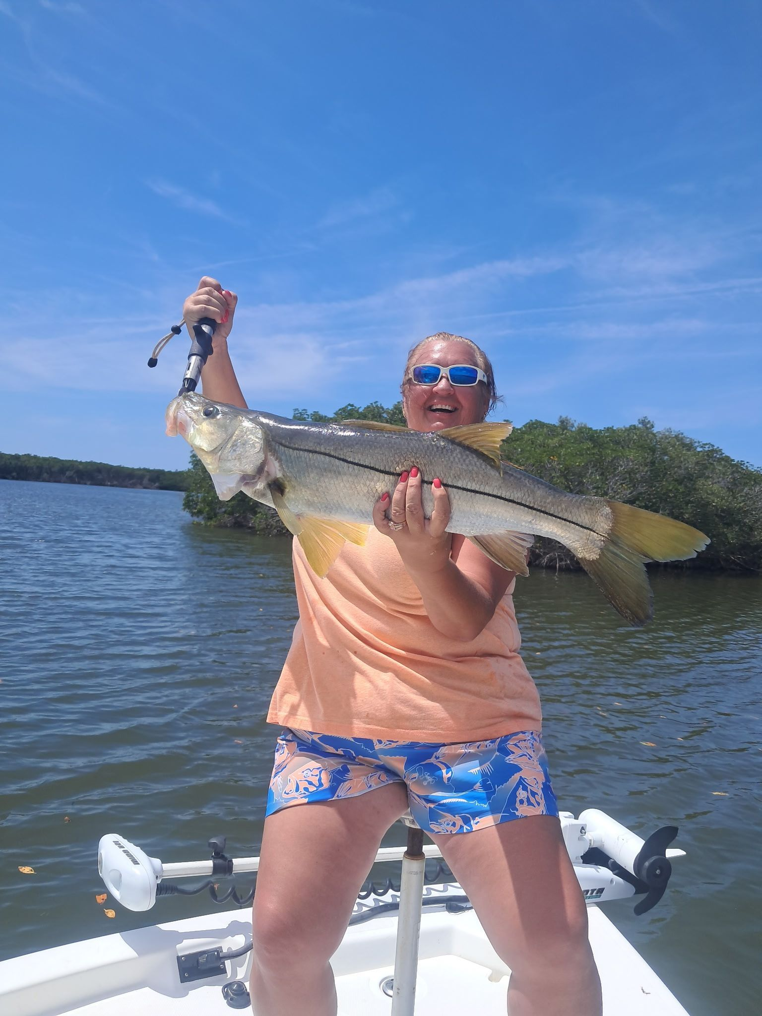 Man on boat holding large redfish, ocean backdrop.