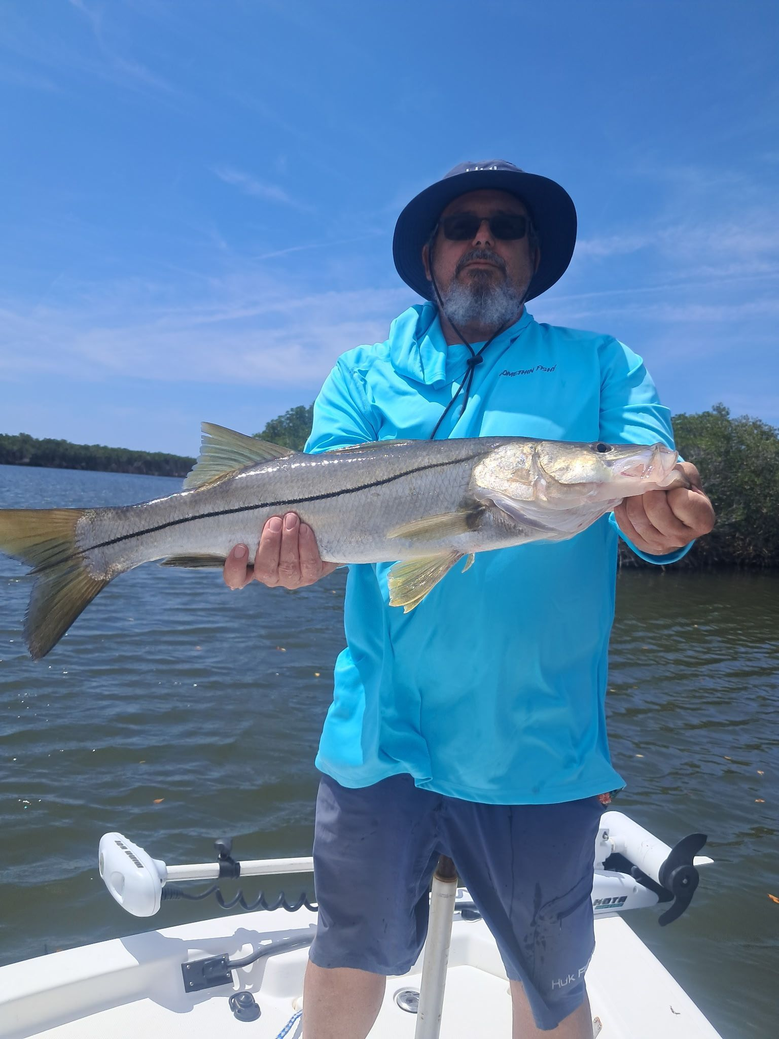 Man holding a silver snook fish on a boat, with a blue sky and water backdrop.