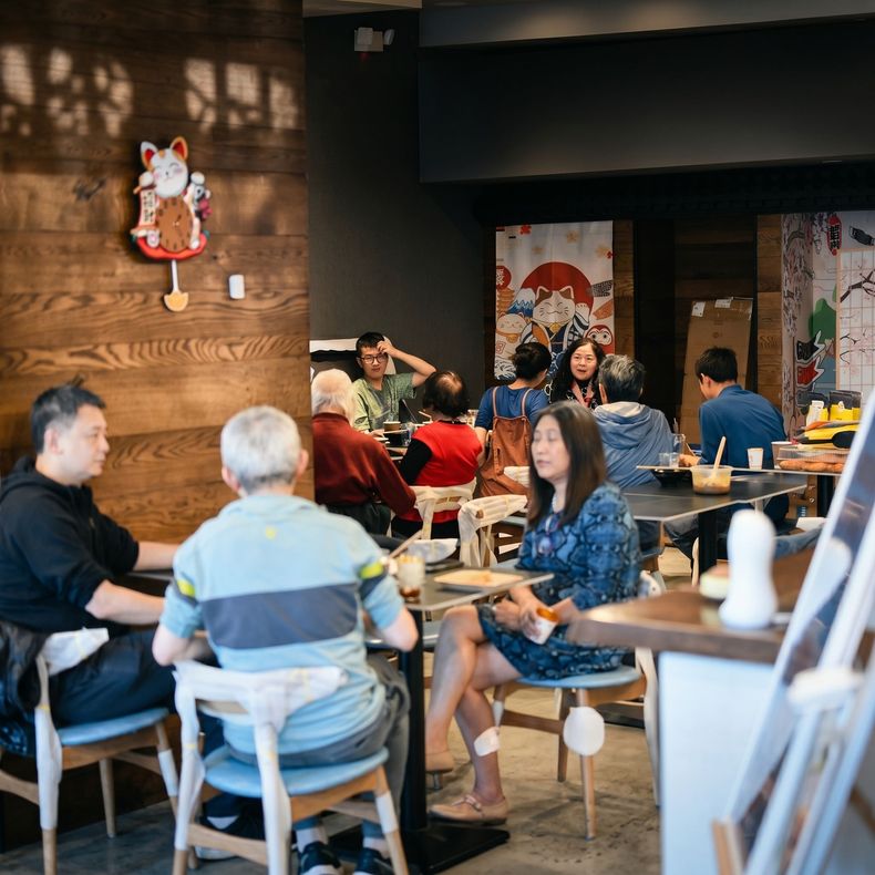 People seated at tables in a cozy café with warm wood walls and hanging decor.