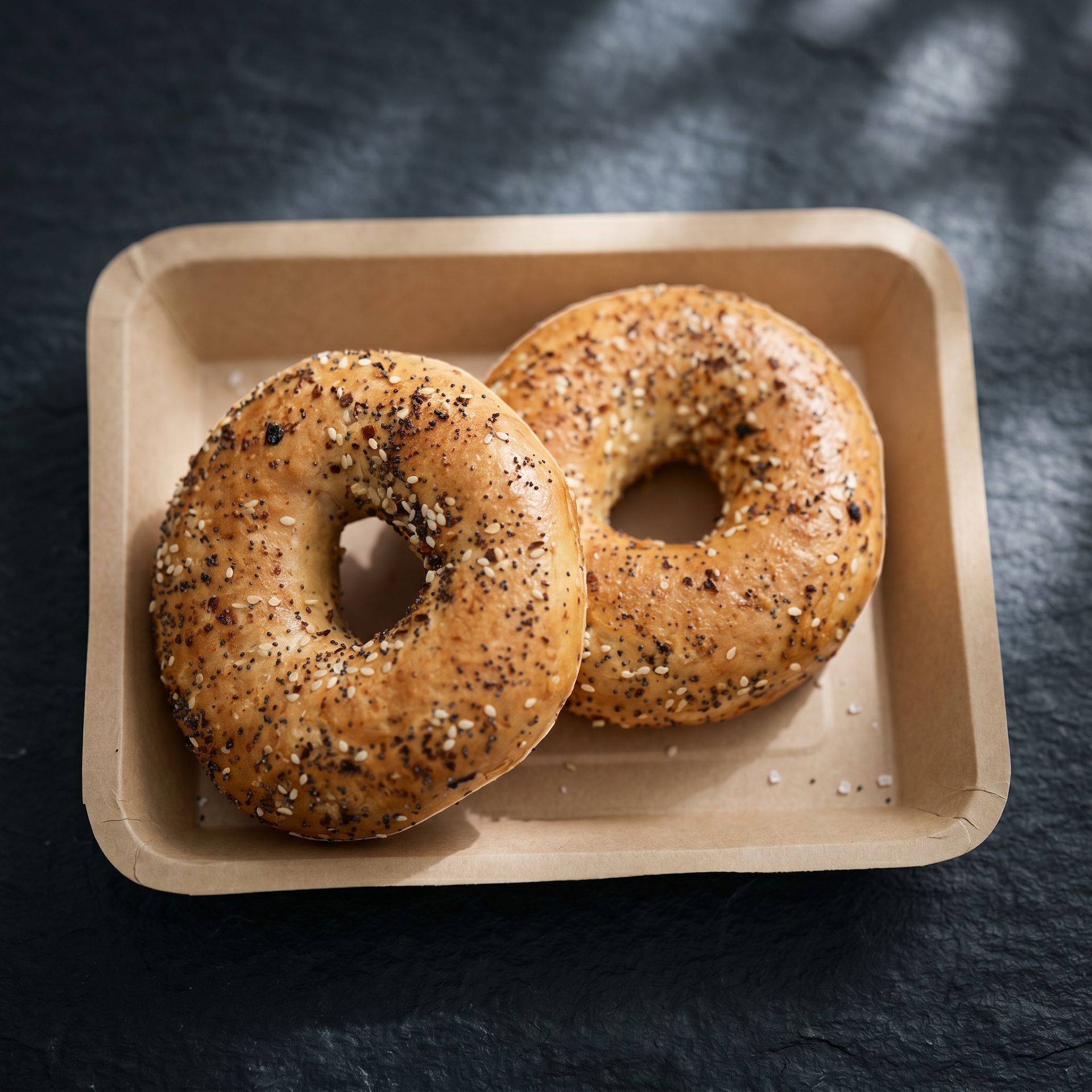 Two sesame bagels in a brown paper tray