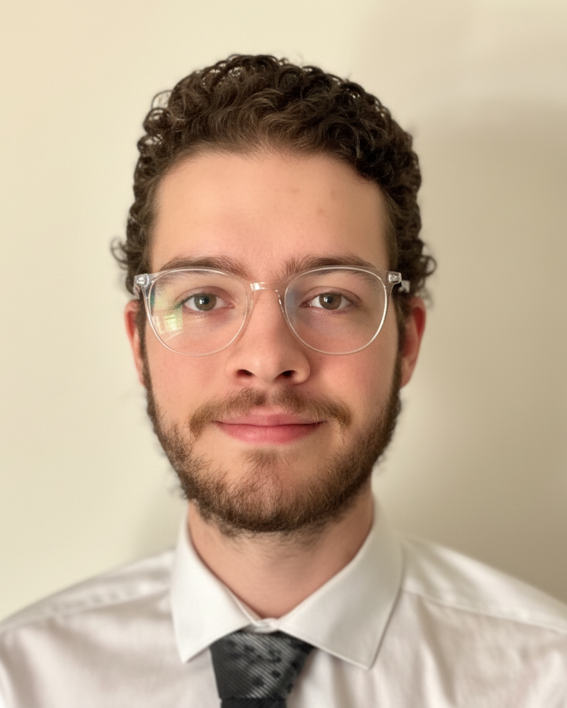 Portrait of a smiling person in glasses, white shirt, and dark tie against a plain beige background