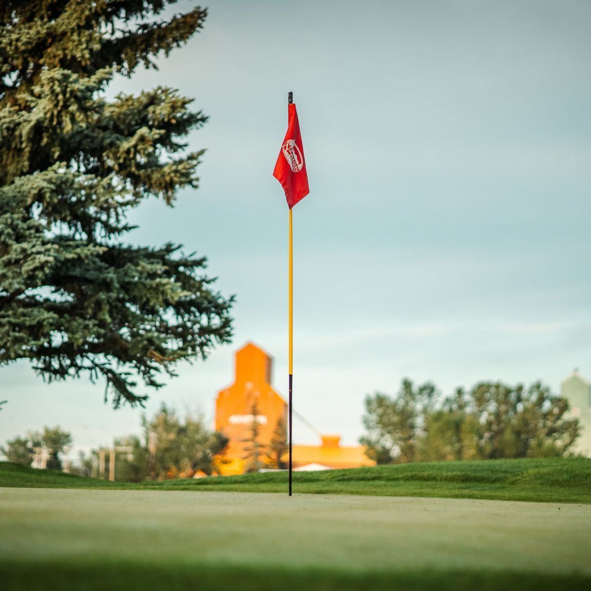 Red flag on a golf green with a blurred orange building in the background.
