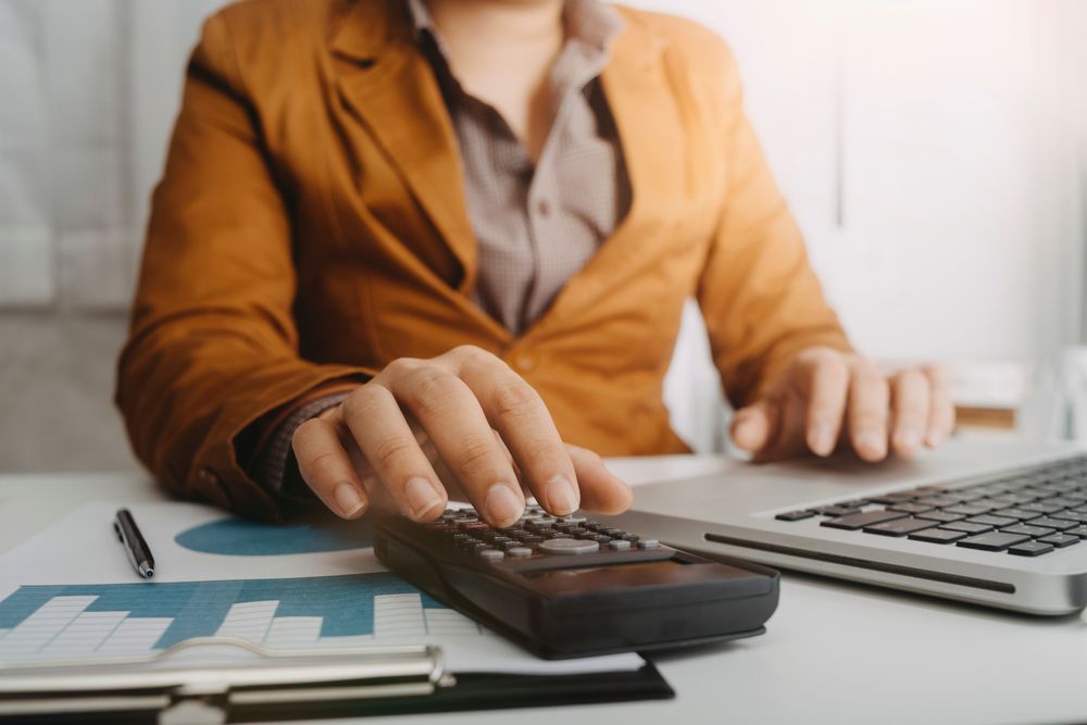 Person using a calculator beside a laptop and documents at a desk — Careful Books in Westcourt, QLD