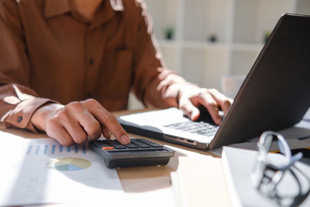 Person using calculator next to laptop on a sunlit desk — Careful Books in Westcourt, QLD