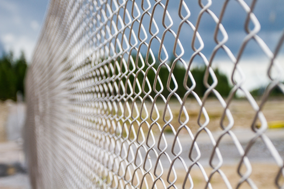 A close up of a chain link fence with trees in the background.