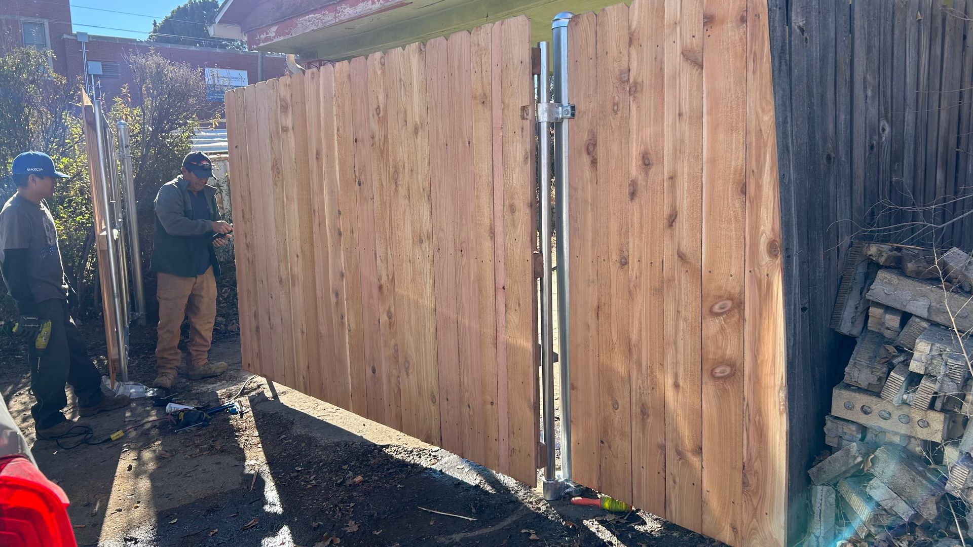 Two workers constructing a wooden fence, with the fence partially built.