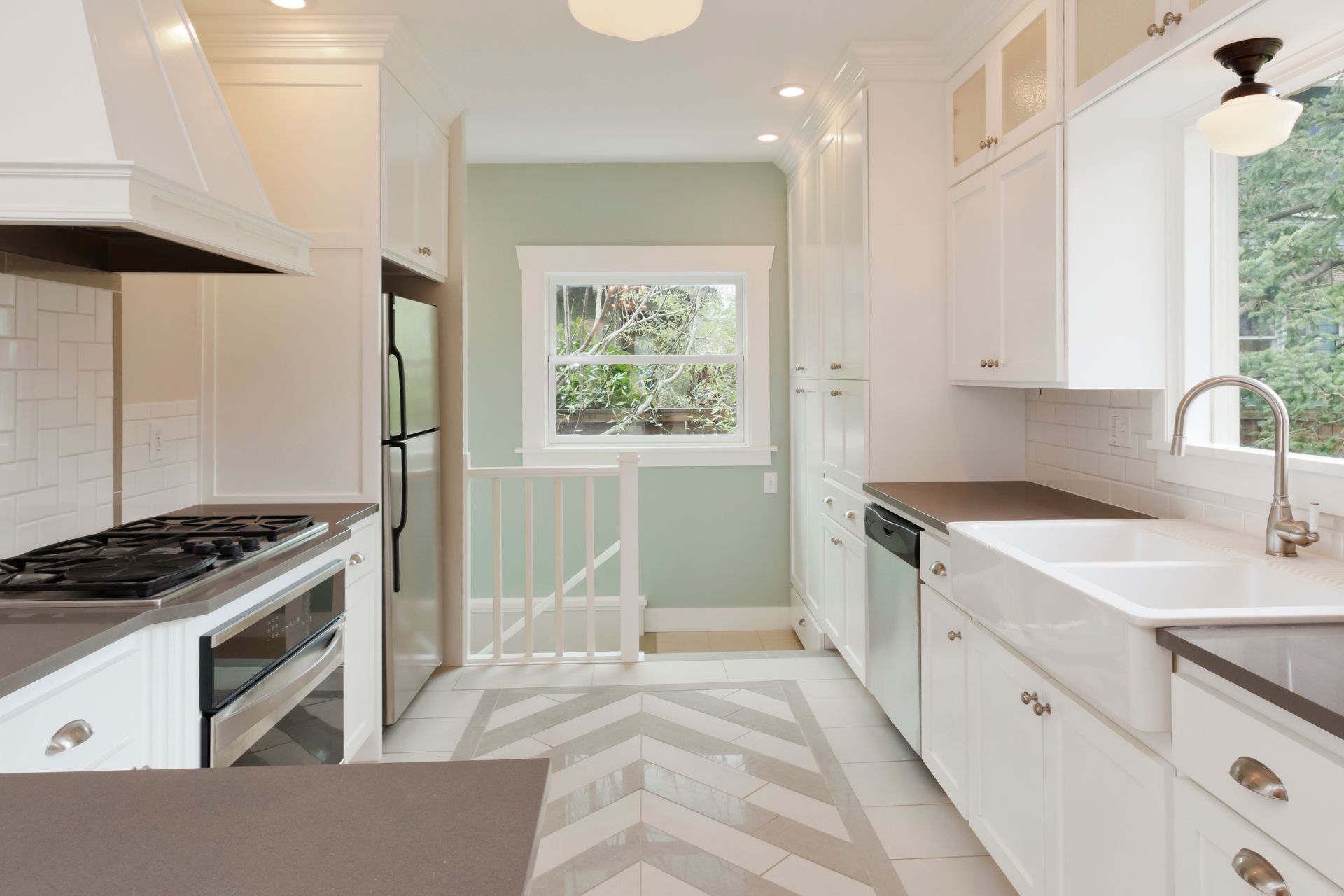 A kitchen with white cabinets , a stove , a sink , and a window.