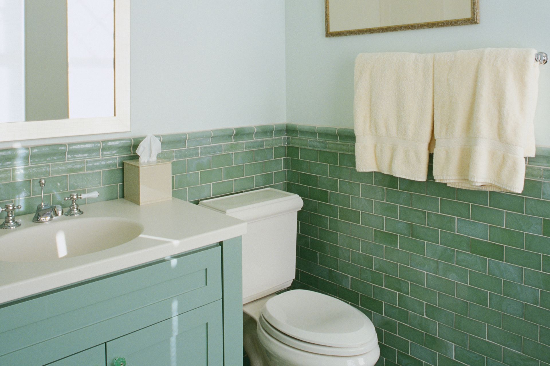 A bathroom with green tiles and a toilet and sink