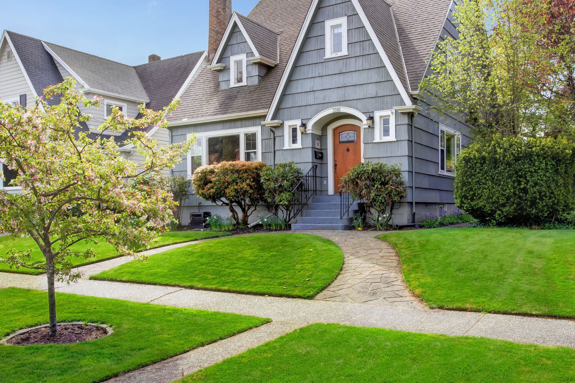 A large gray house with a red door and a lush green lawn.