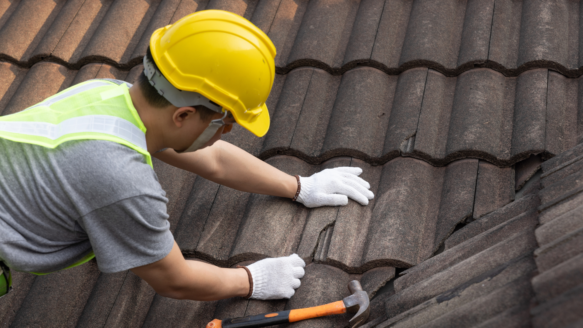 A man wearing a hard hat and gloves is working on a roof with a hammer.