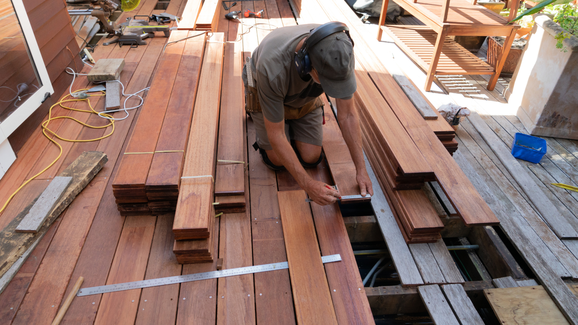 A man is measuring a piece of wood on a deck