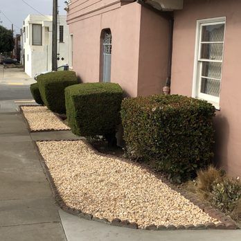A sidewalk with bushes and gravel in front of a house