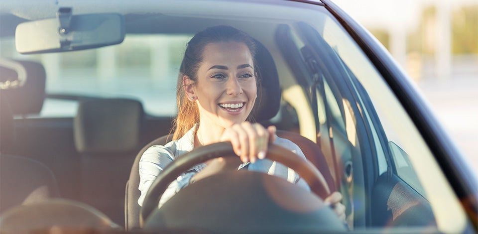 Smiling driver holding the steering wheel inside a sunlit car