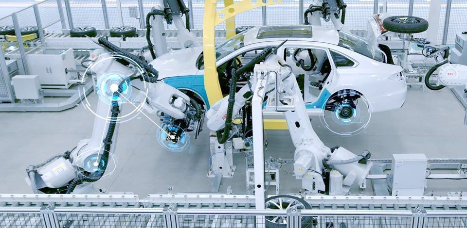 Robotic arms assembling white car bodies on an automotive factory line