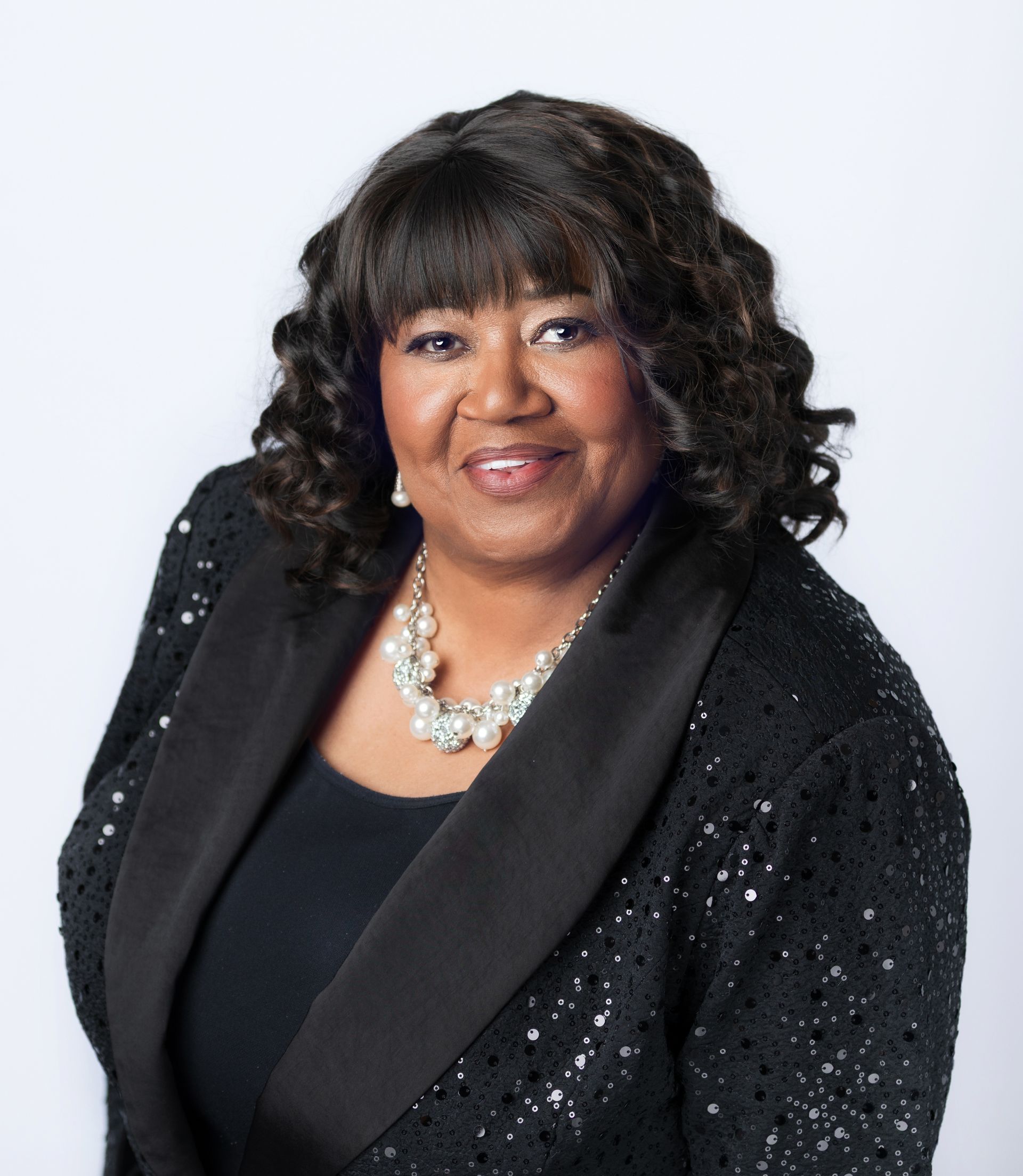 A woman wearing a black jacket and necklace smiles for the camera