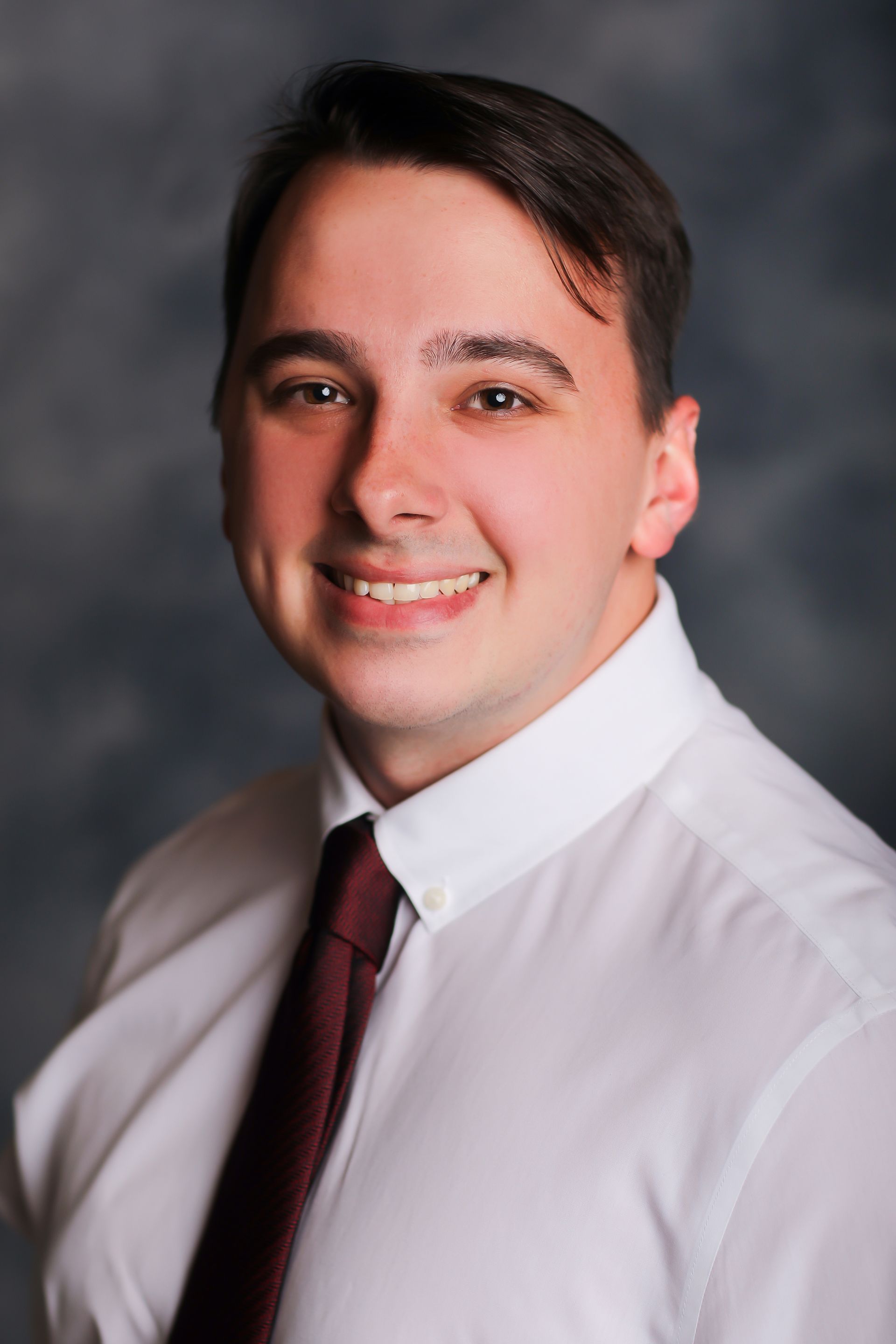 A young man in a white shirt and red tie is smiling for the camera.