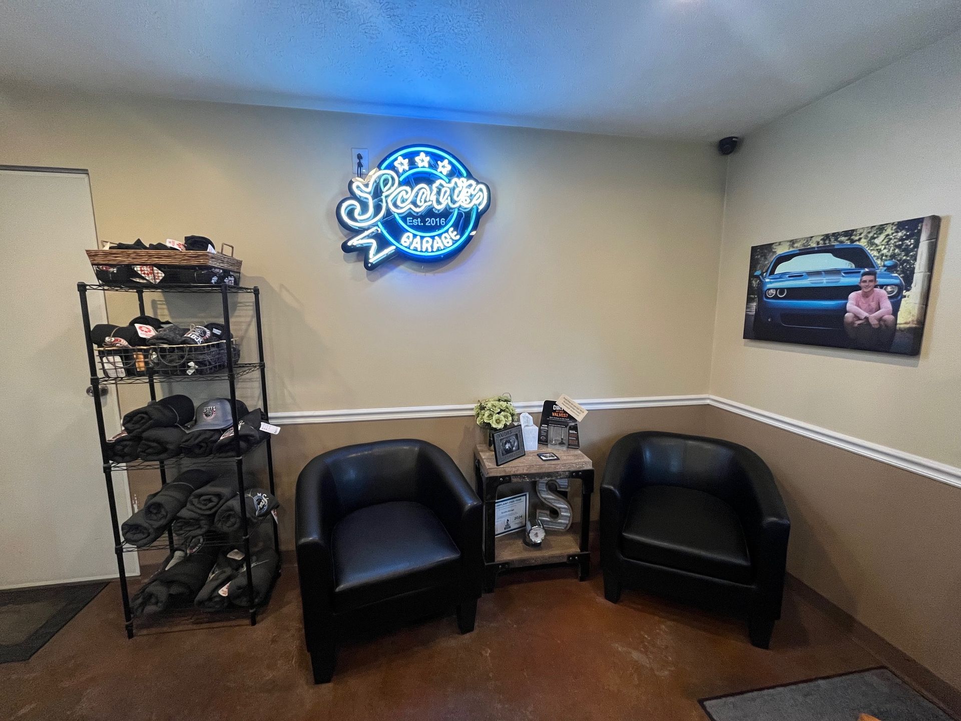 Waiting room with black chairs, shelving with merchandise, neon sign, and photo. | Scott's Garage