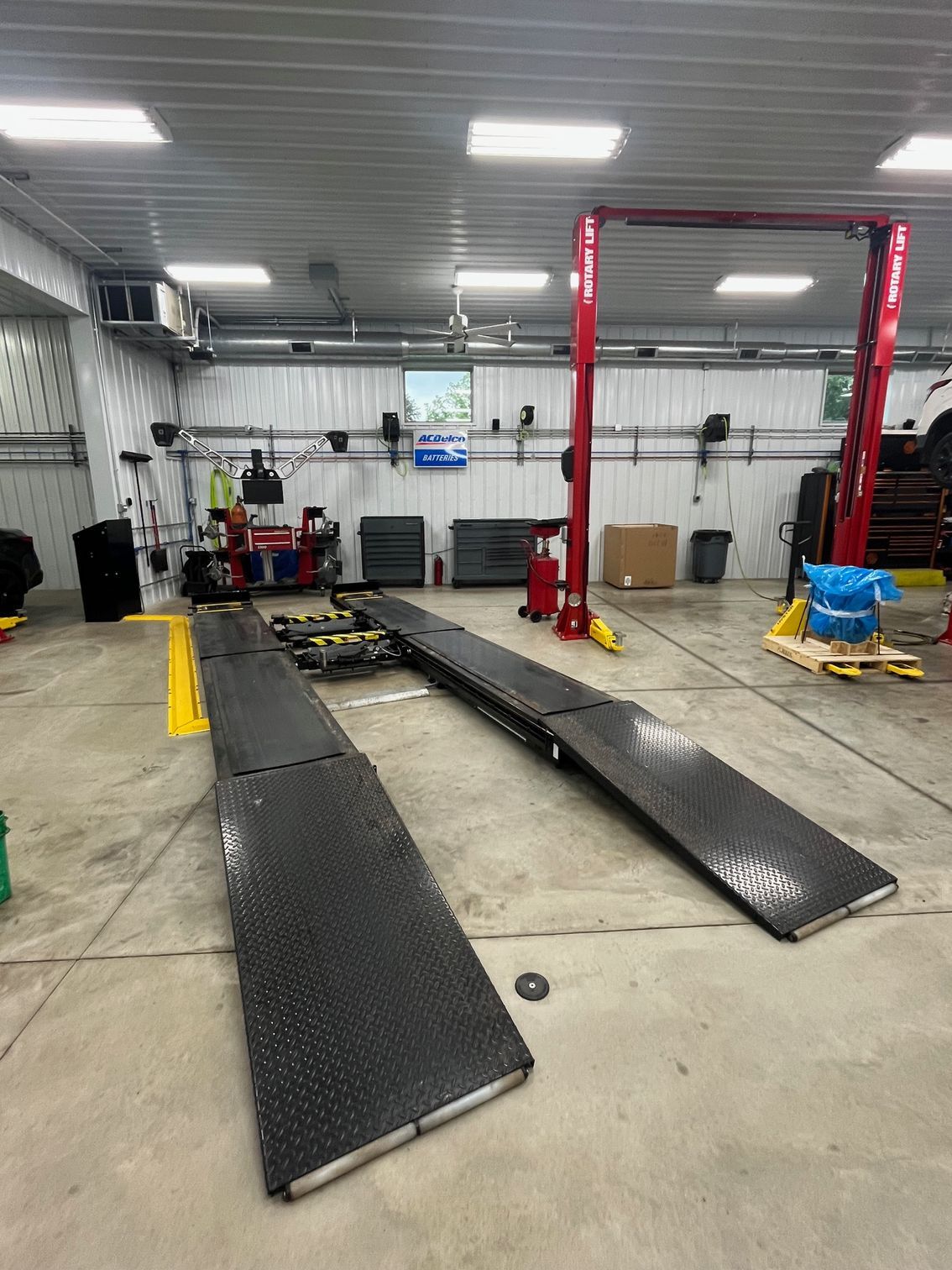 Car lift in a mechanic shop; ramps on the floor, red lift columns, tools, and a vehicle being serviced. | Scott's Garage