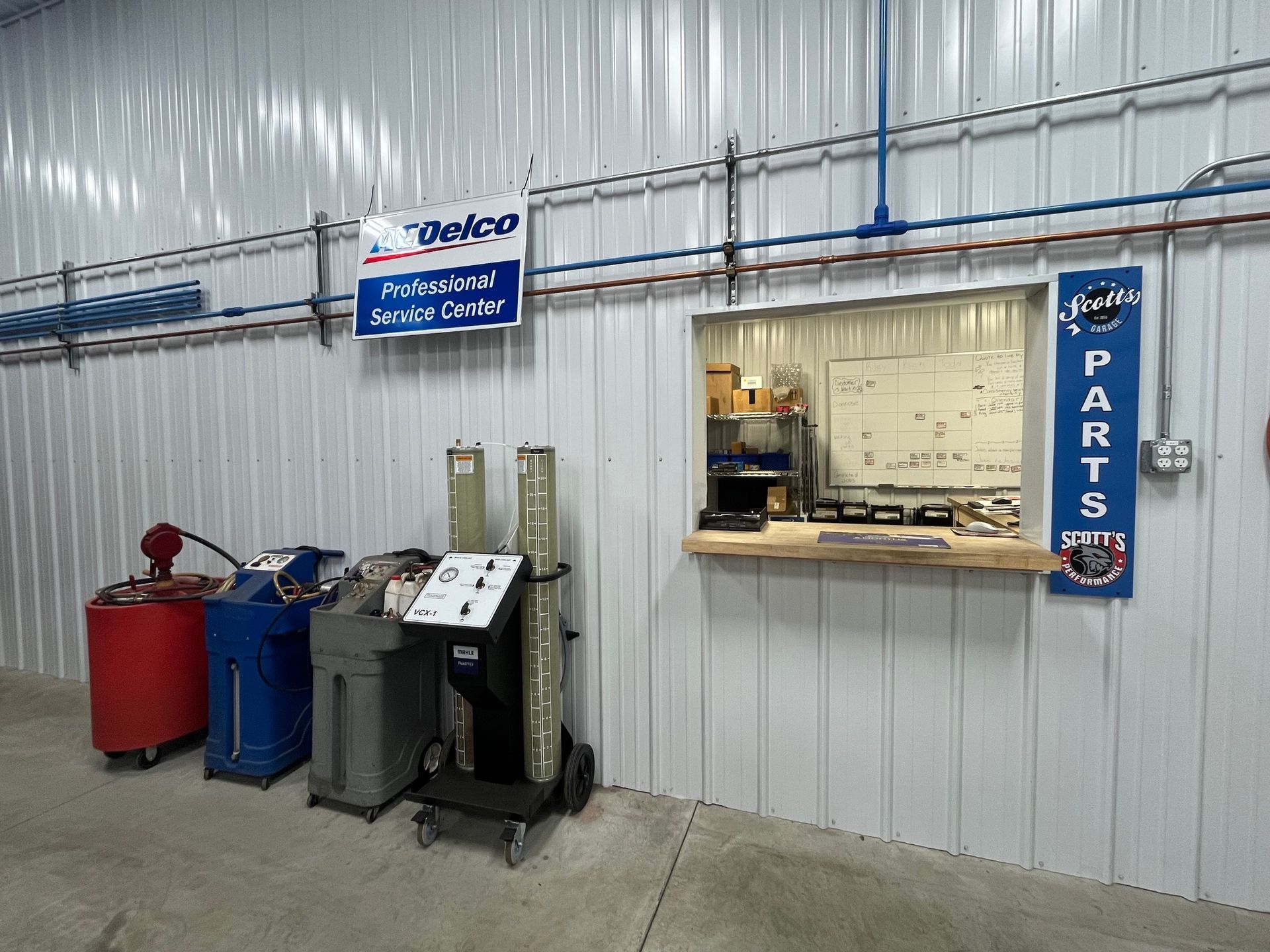 A vehicle service station with parts, equipment, and a window counter with a whiteboard and tools. | Scott's Garage