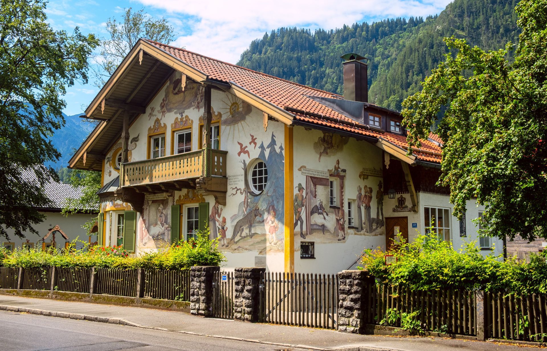 Traditional Bavarian house decorated with painted murals, surrounded by greenery and Alpine mountains