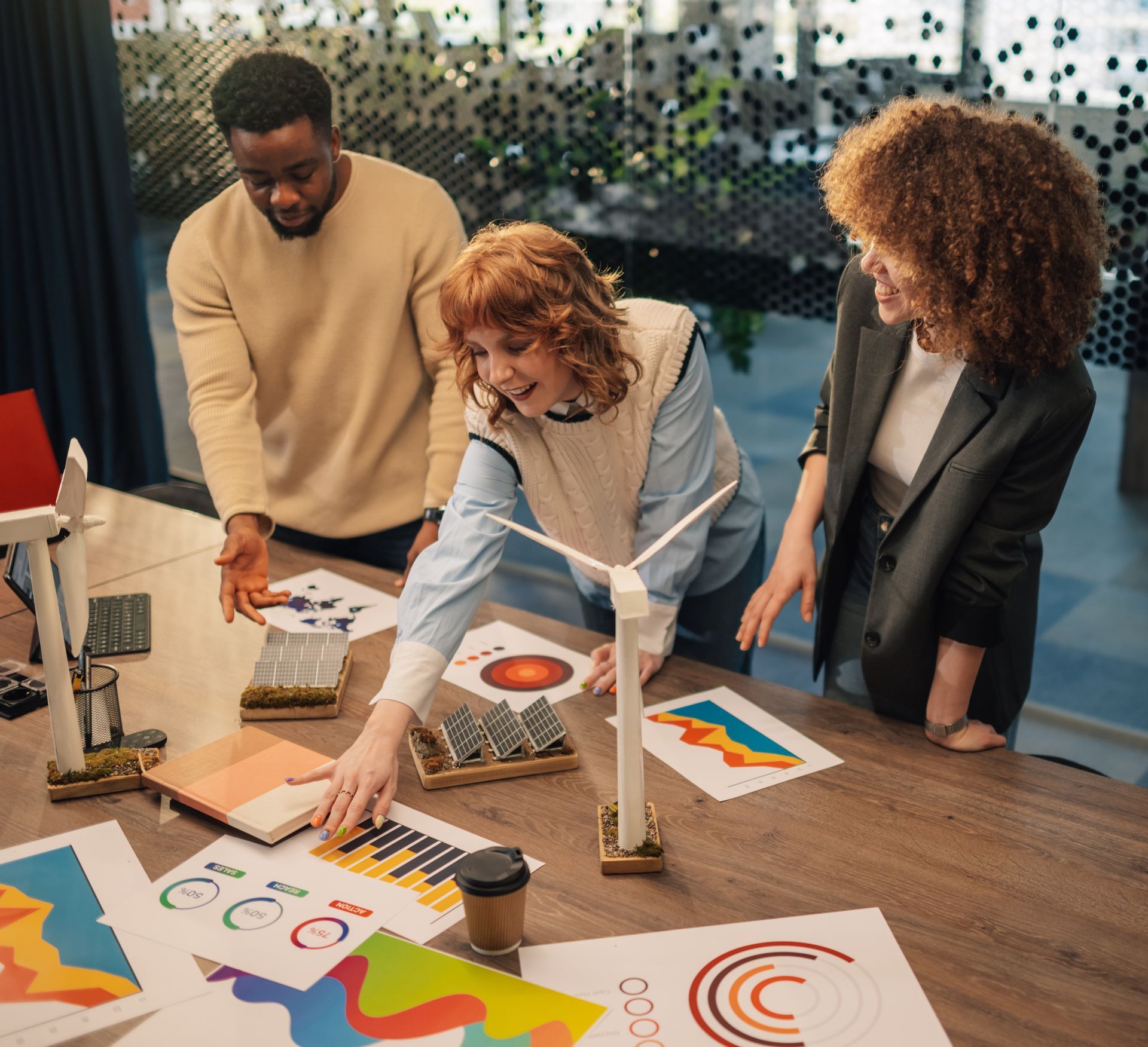Three people collaborating around a table with diagrams and models of renewable energy sources.