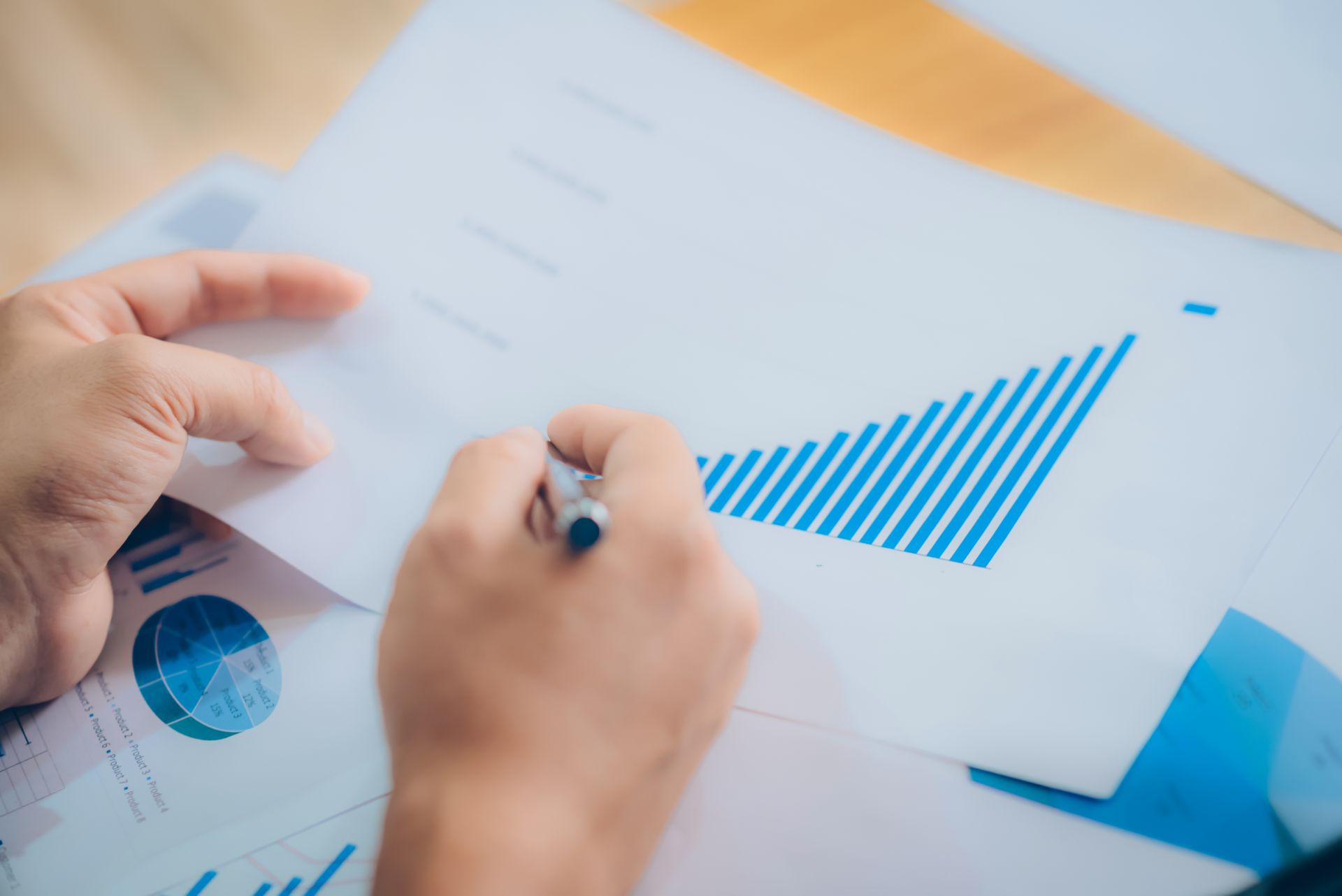 Hands writing on a report with blue charts and graphs on a desk
