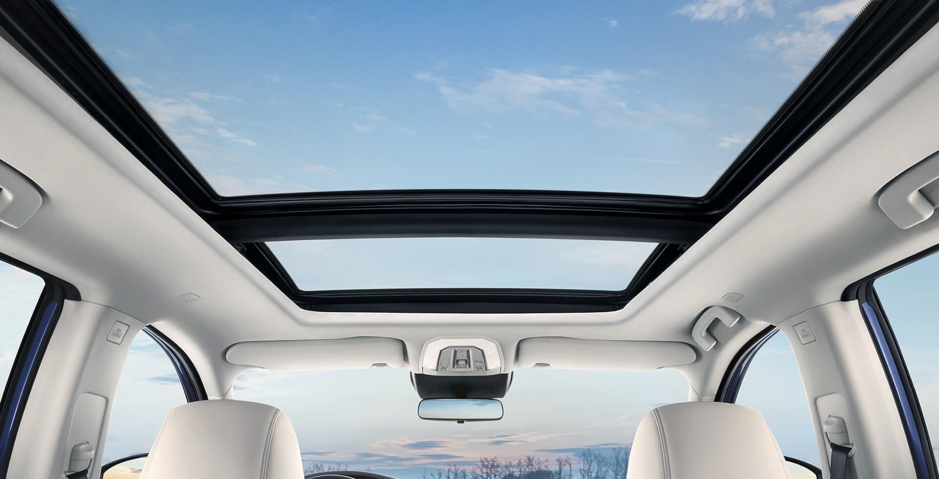 Interior car view with open sunroof, showing blue sky, white seats, and rearview mirror.