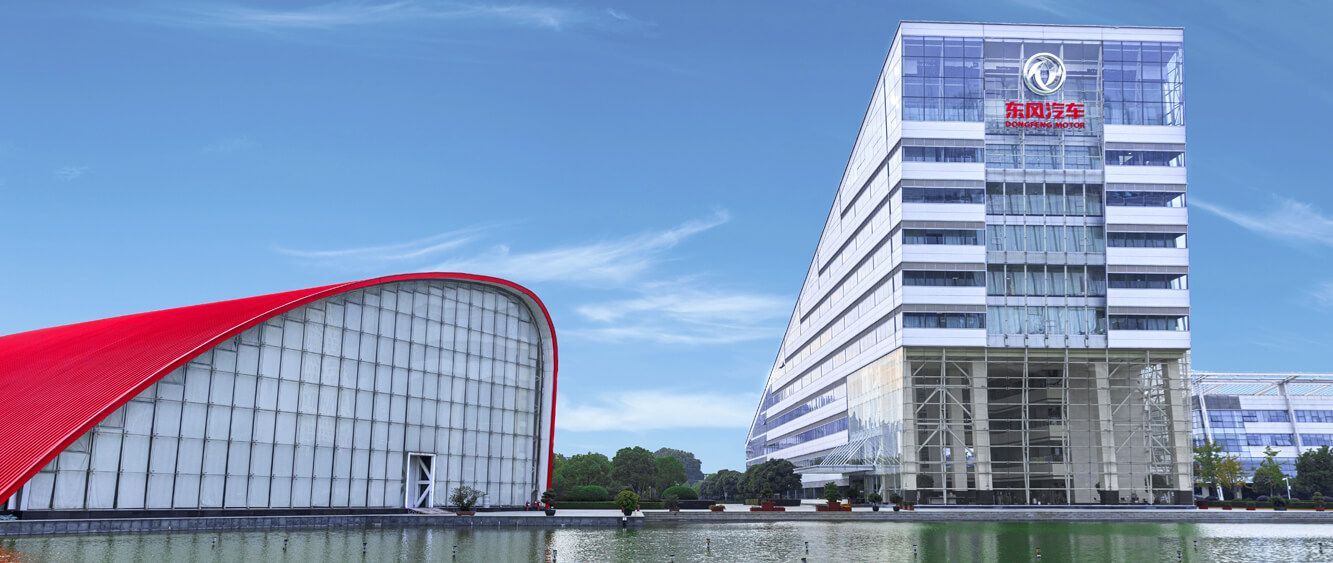 Buildings with a red curved roof and a tall, white building with a logo, by a lake.