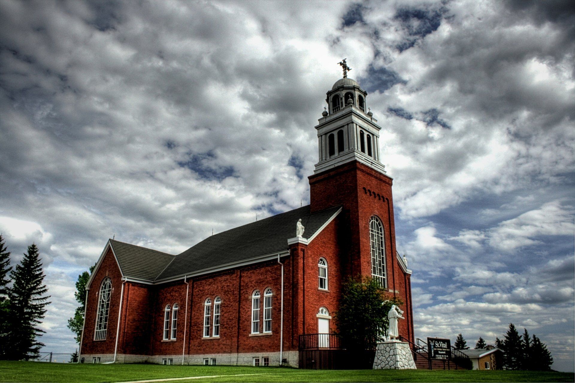 A large red brick church with a steeple and a cross on top.