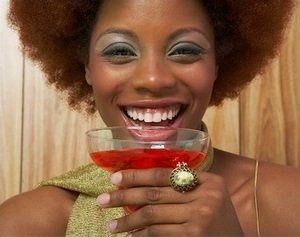 A woman is smiling while holding a glass of red liquid