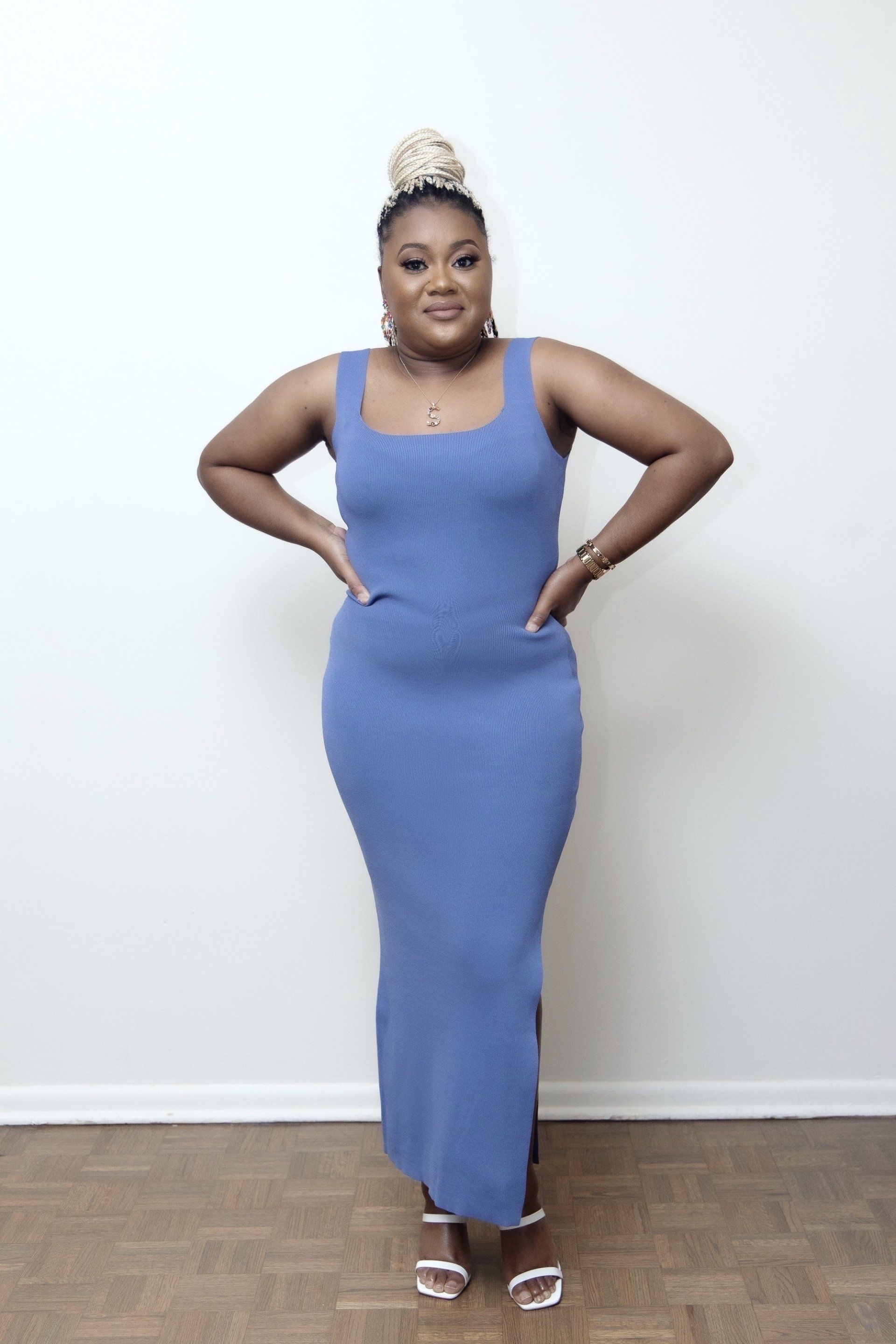A woman in a blue dress is standing with her hands on her hips.