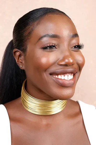A woman wearing a gold choker necklace is smiling.