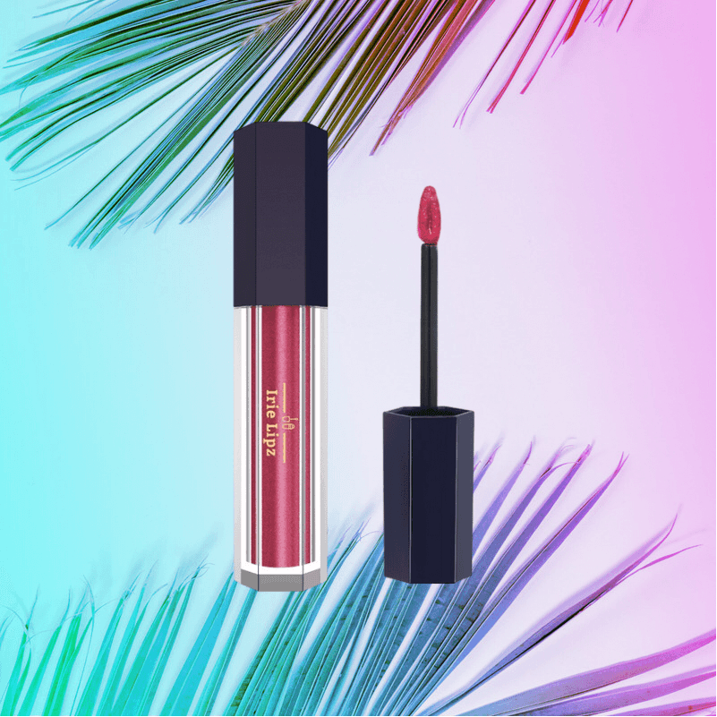 A bottle of liquid lipstick with a brush next to a palm tree leaf.