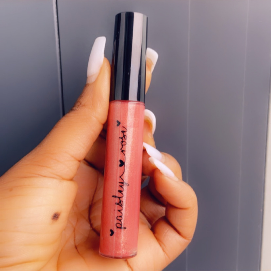 A woman is holding a pink lip gloss in her hand