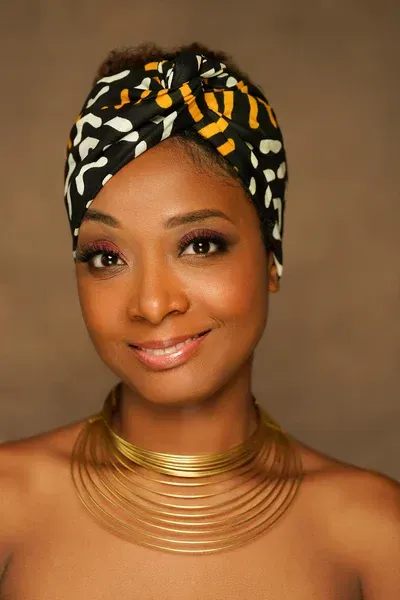 A woman wearing a turban and a gold necklace is smiling.