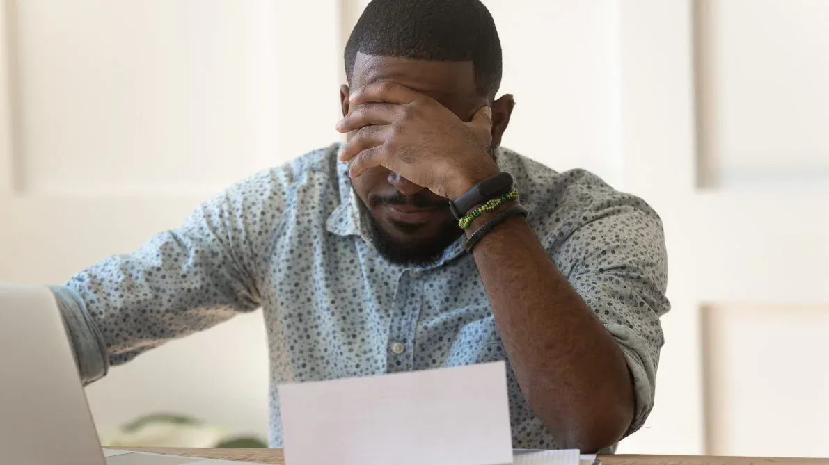 A man is sitting at a desk with a laptop and a piece of paper.