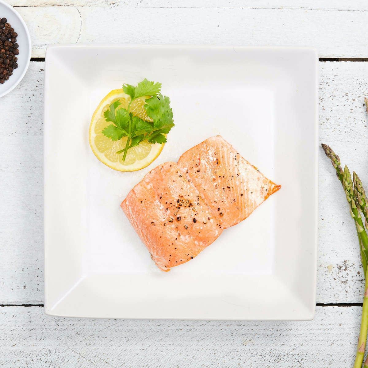 A piece of salmon on a white plate with lemon and cilantro