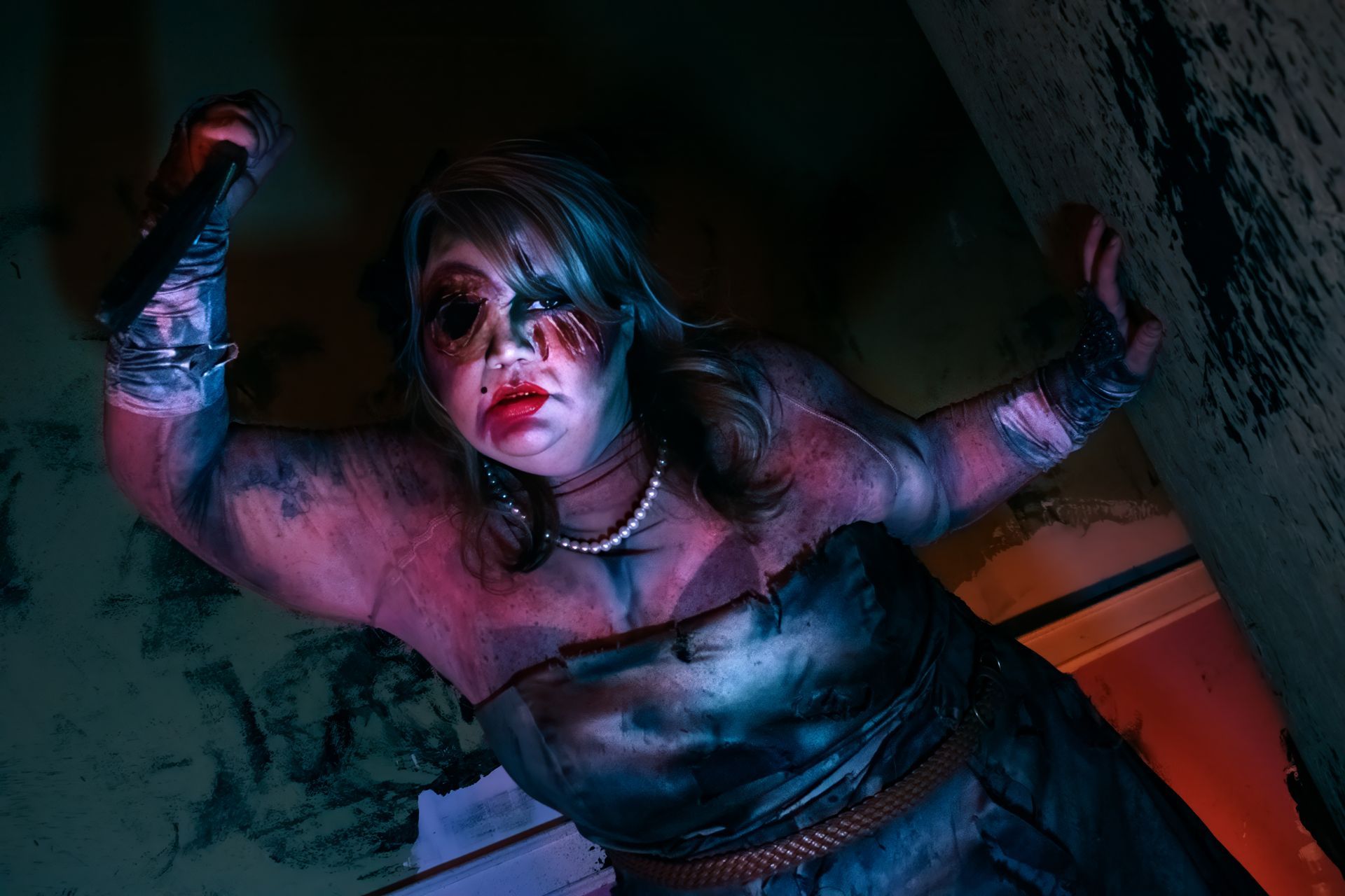 Bloody woman holding kife, wearing a dark outfit in dramatic red and blue lighting.
