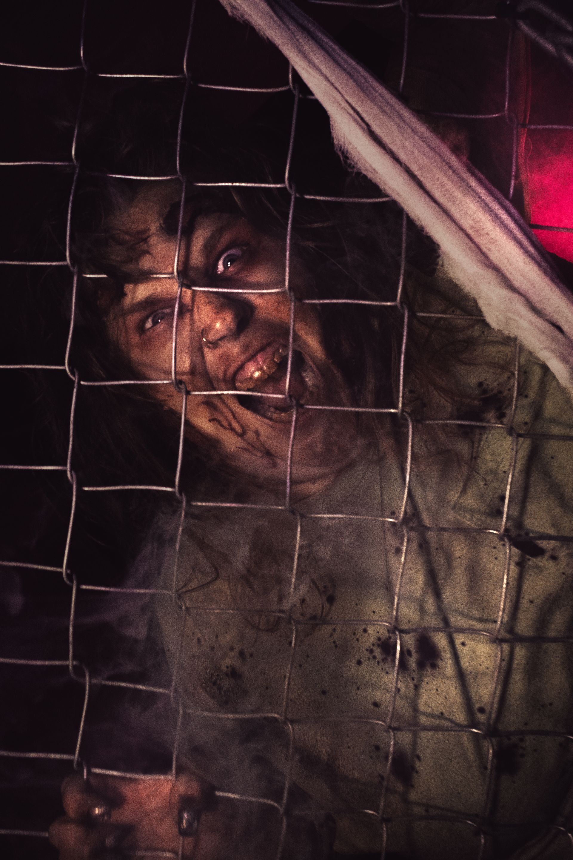 Man with a bruised face behind a wire fence in dim light, looking distressed