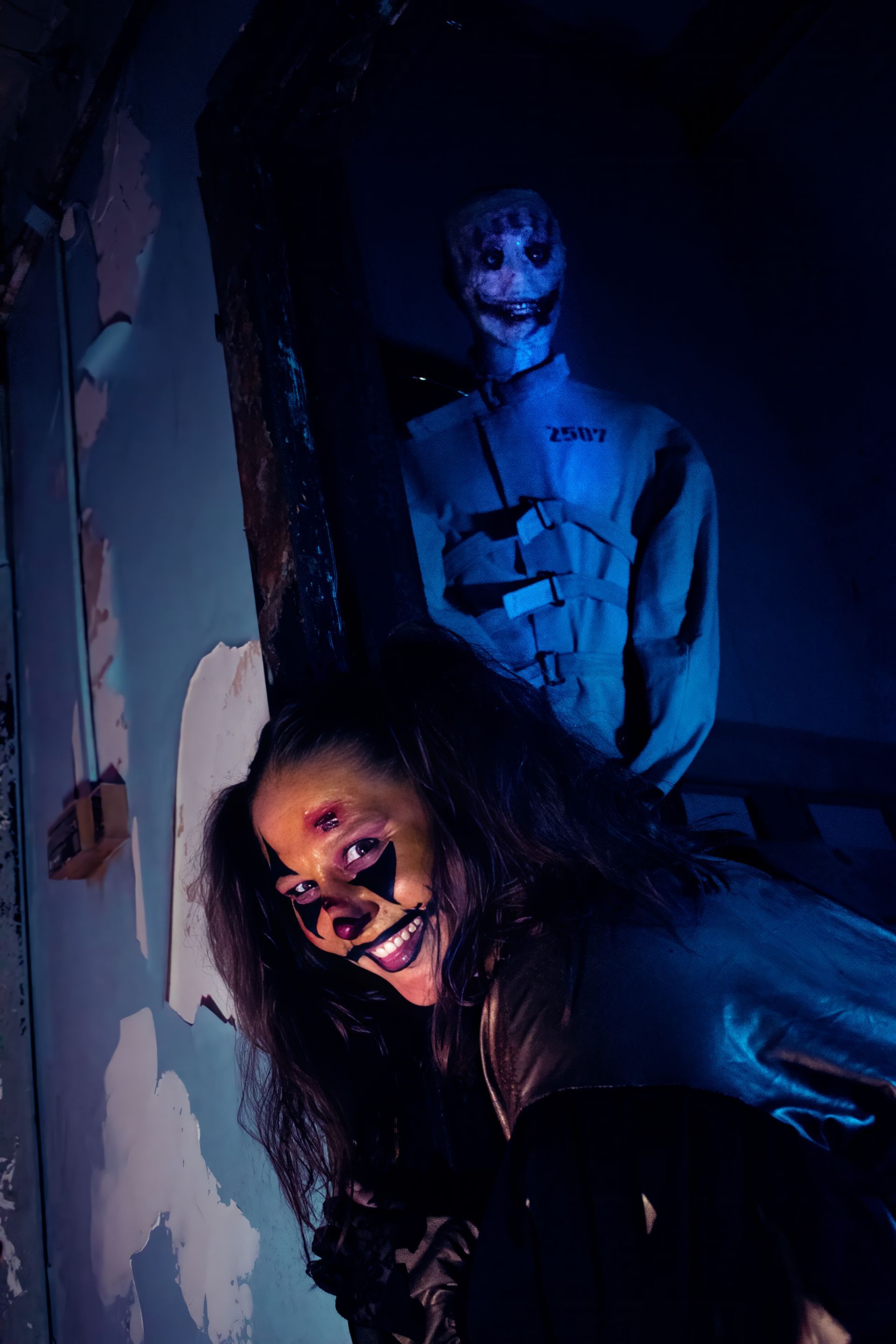 Blue-lit horror scene: two eerie figures in a dark hallway, one crouching in front, one standing behind.