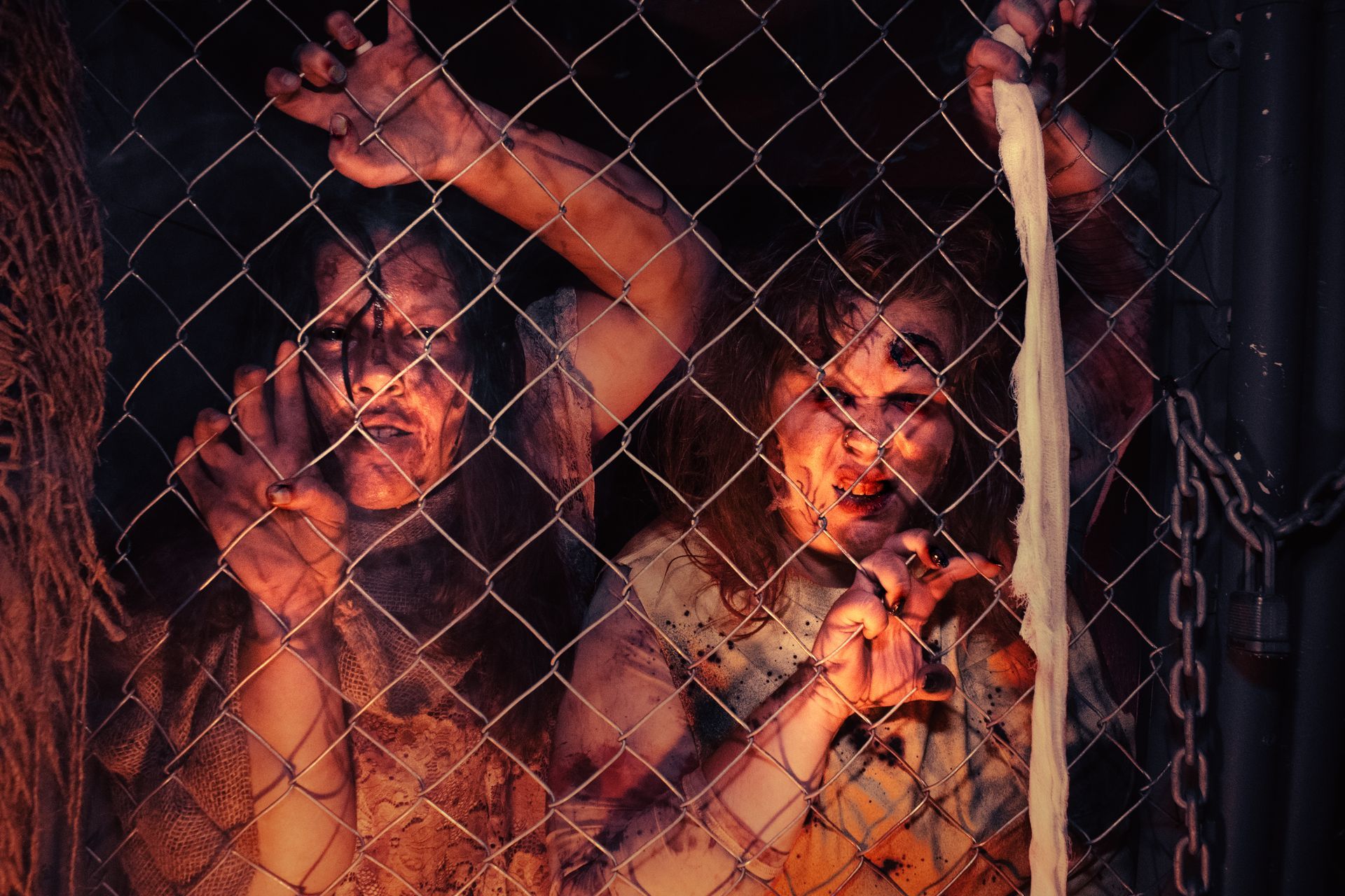 Two people behind a chain-link fence, lit by red light, looking out with intense expressions