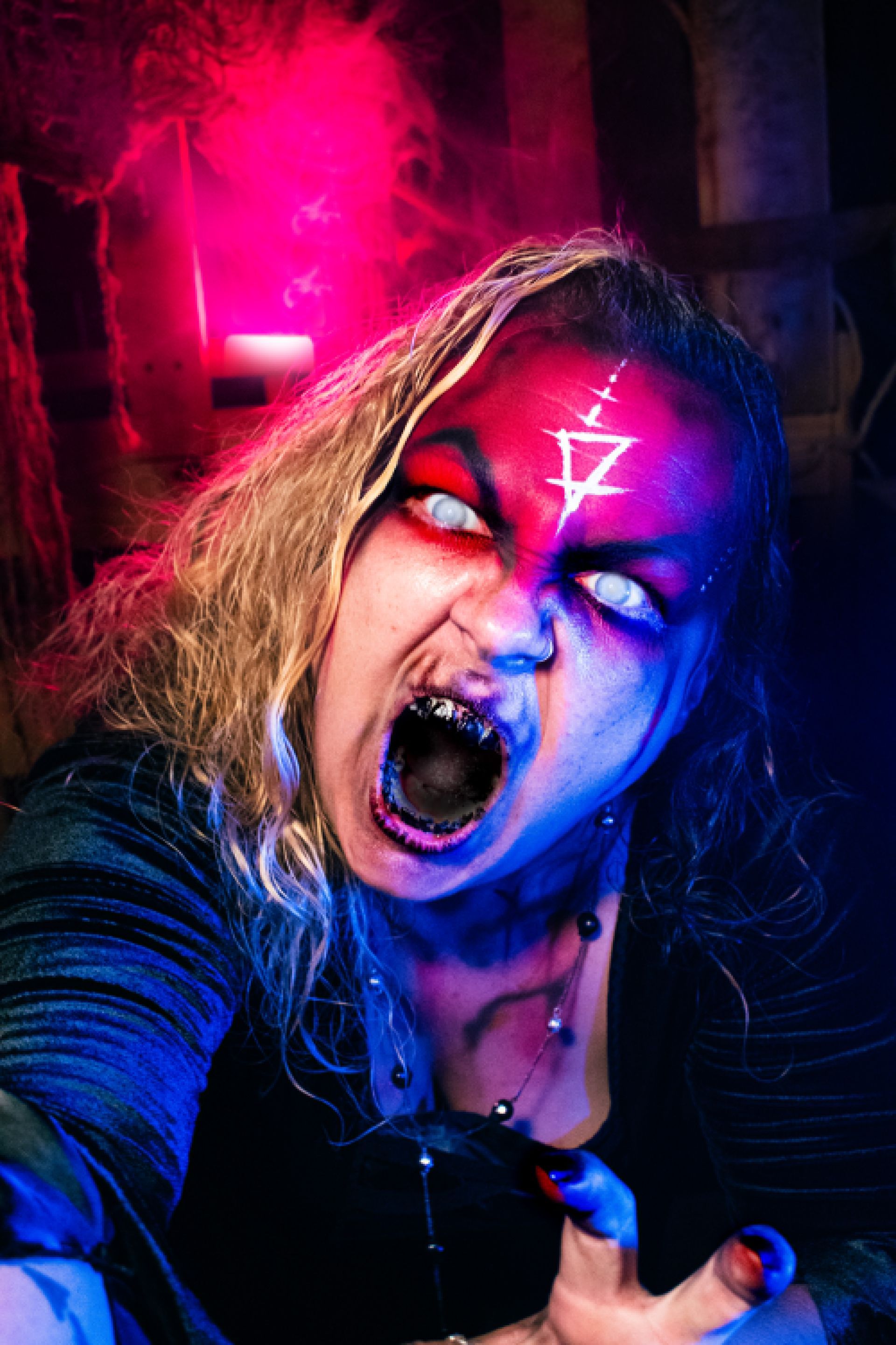 Person with dramatic blue face paint, shouting in neon-lit scene