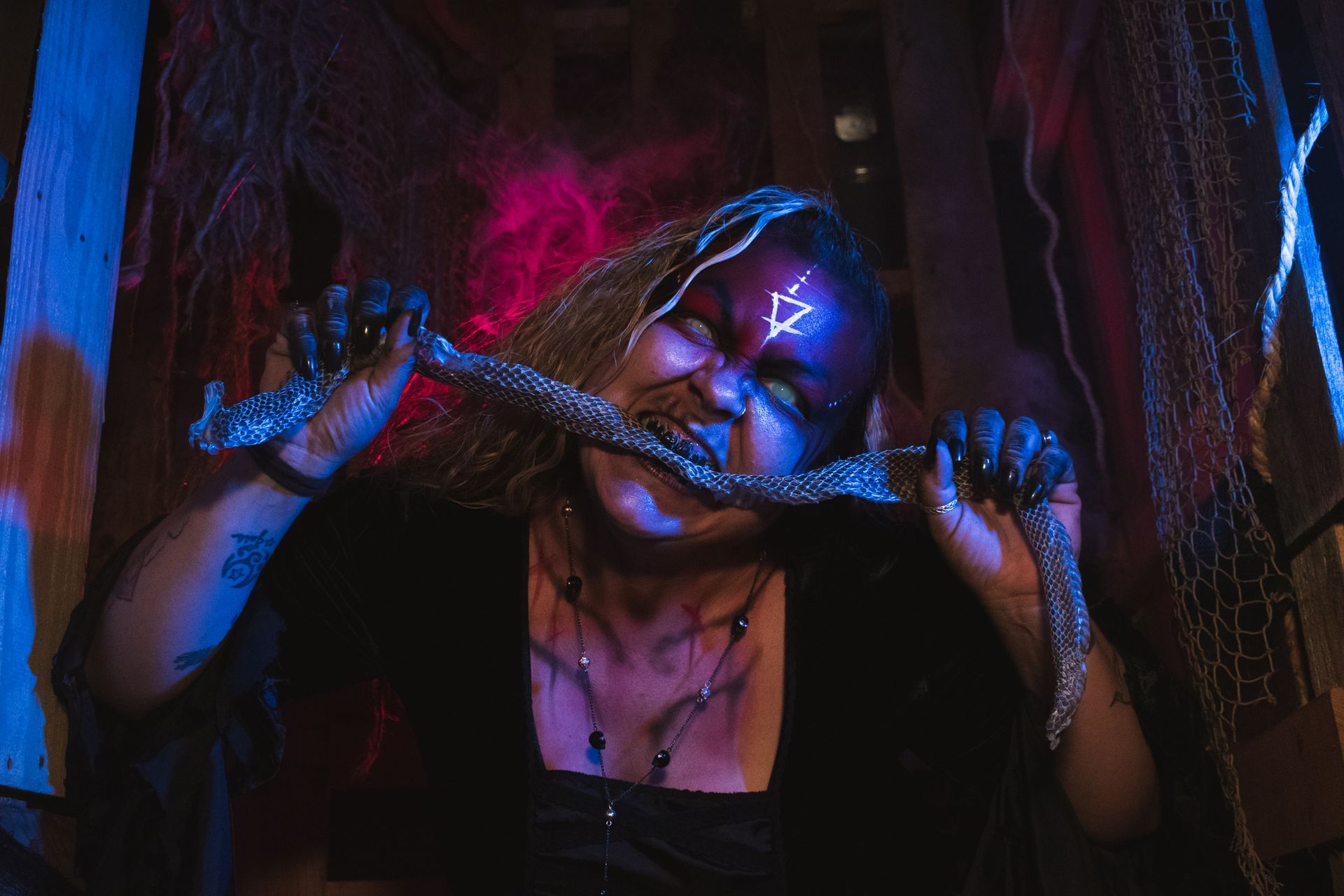Person in a dark neon-lit setting biting into chain, with blue and pink light effects