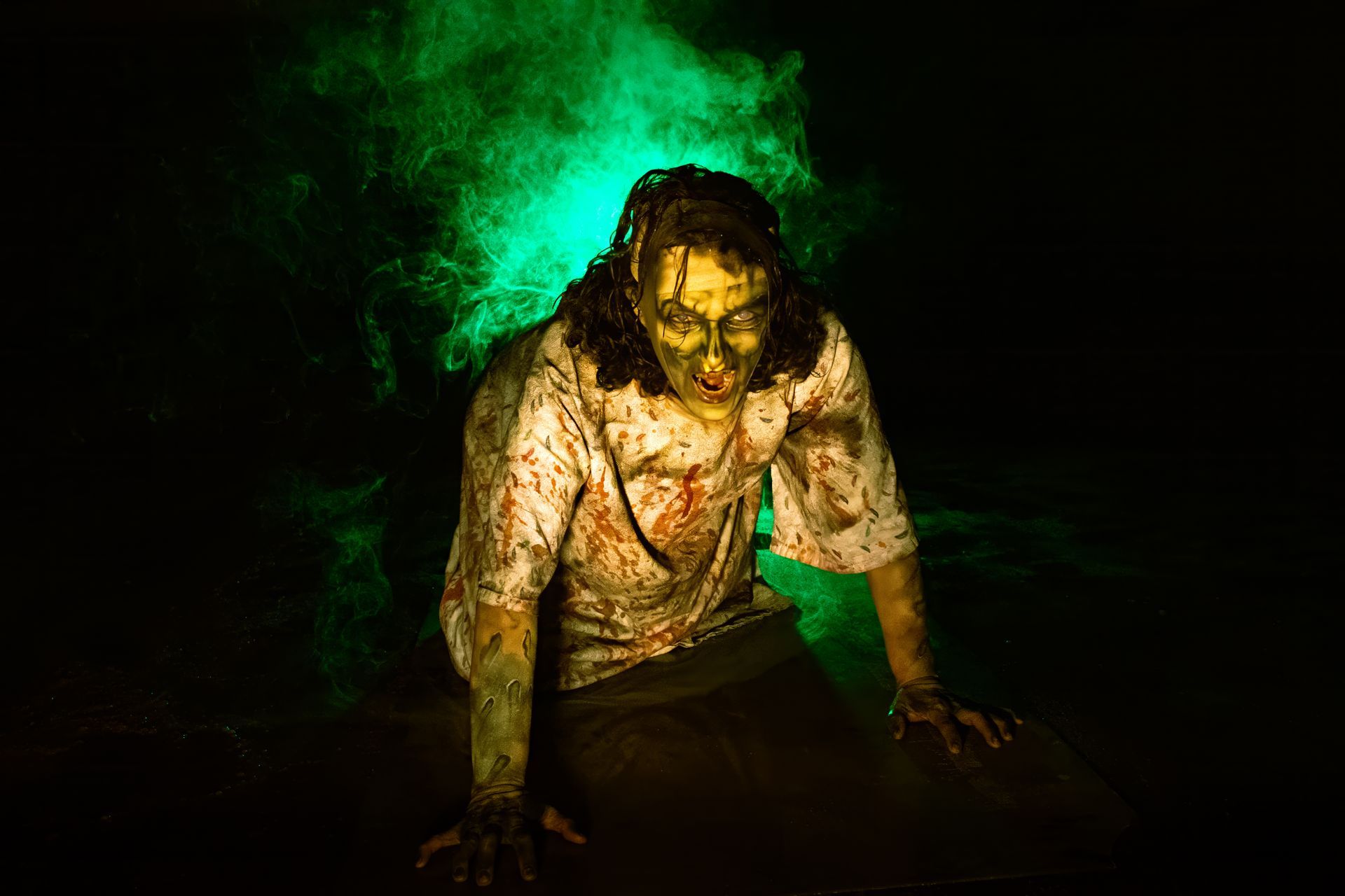 Bloodied figure crawling in darkness, lit by eerie green smoke