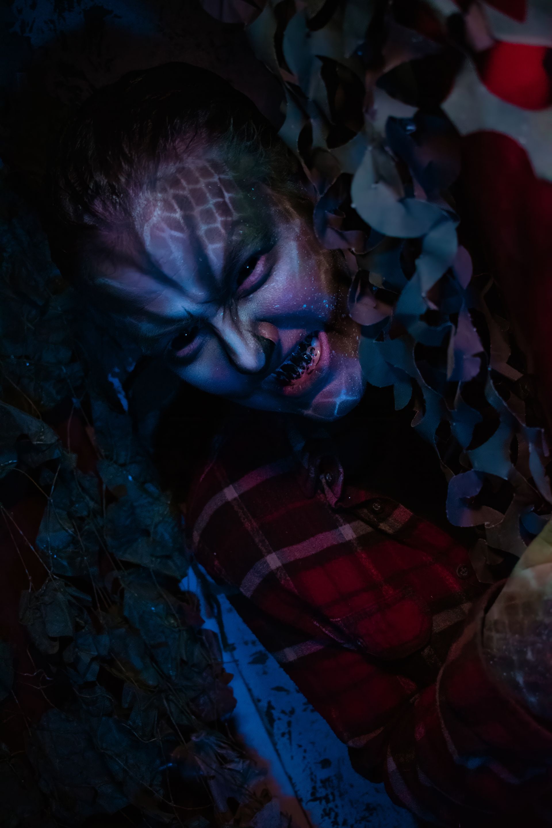 Person in dark makeup in moody blue-red lighting.