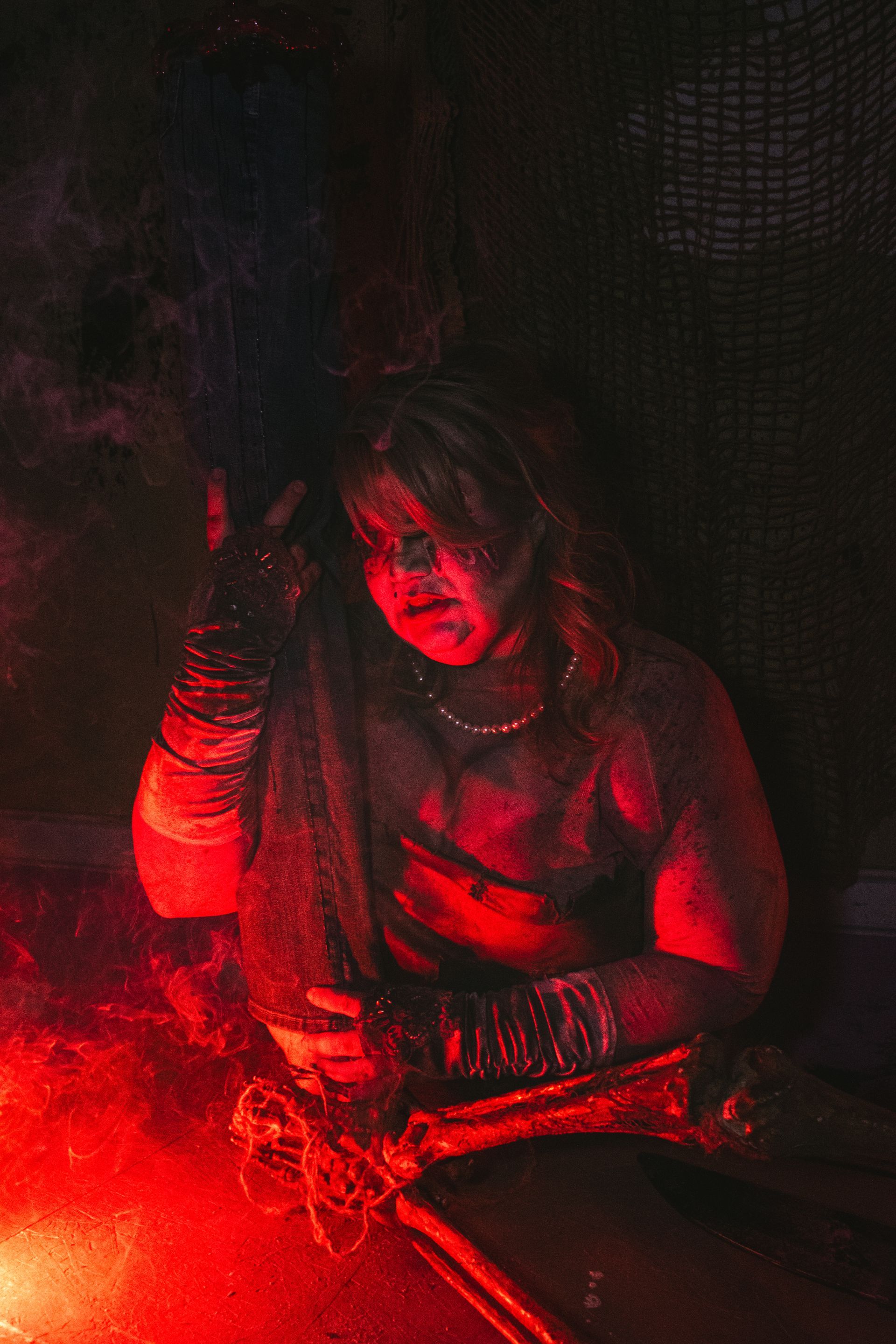 Person lit by red light sitting in a dark space, holding an object with a serious expression.