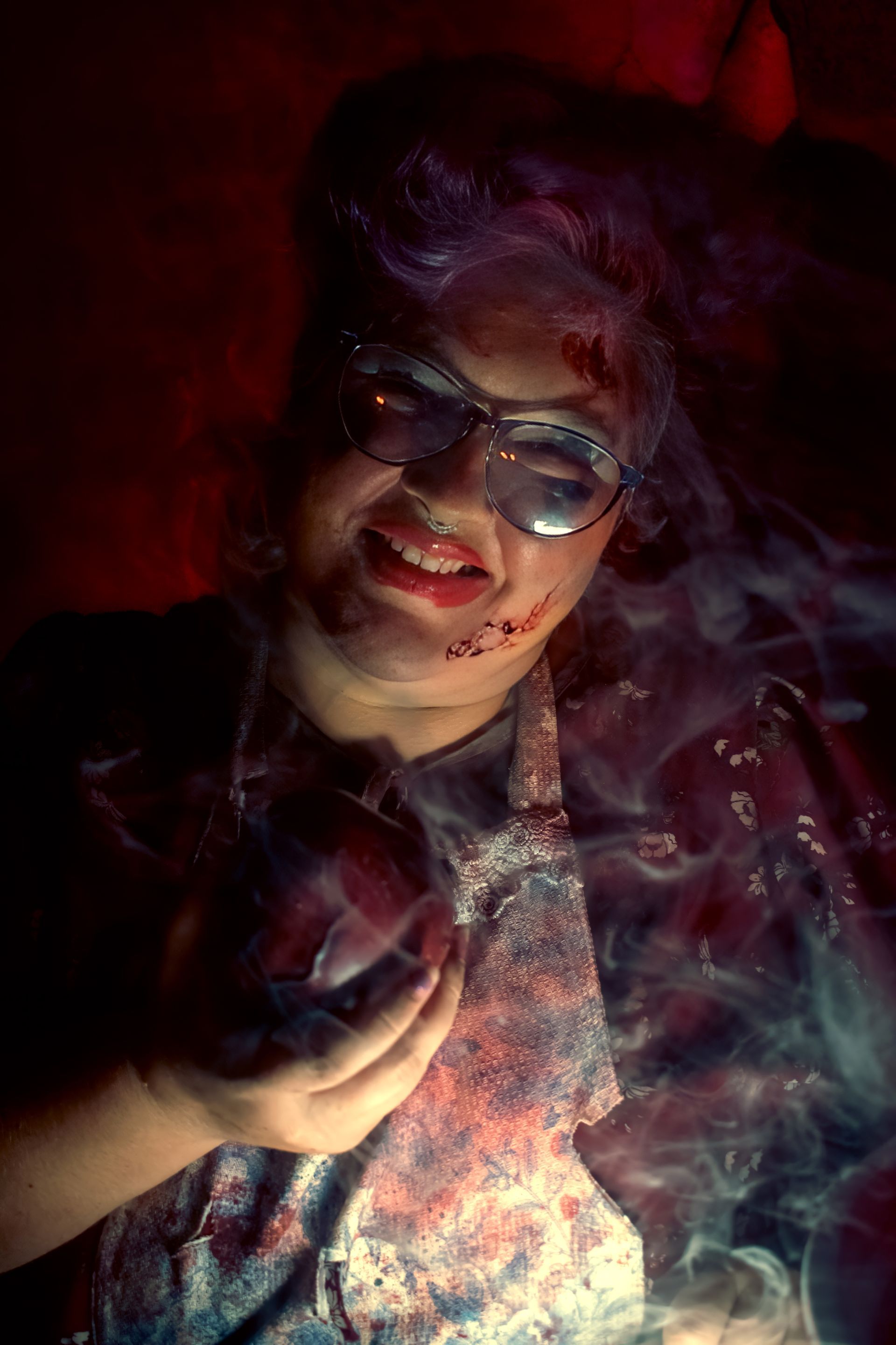 Person with glasses in a dark red-lit setting, smiling amid swirling smoke and colorful light.